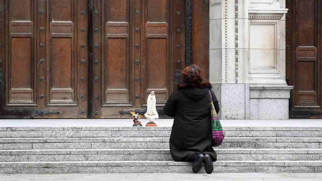 donna che prega davanti a una chiesa chiusa