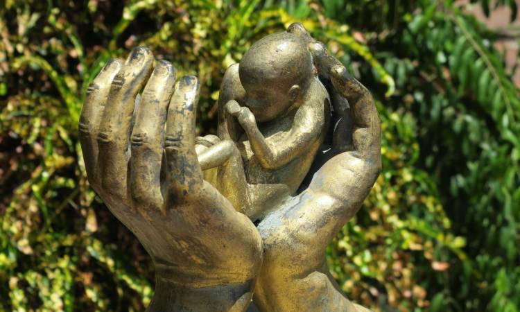statua di un bimbo fra due mani