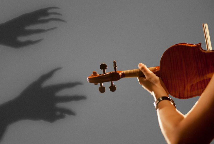 ragazza che suona il violino e dietro di lei mani demoniache