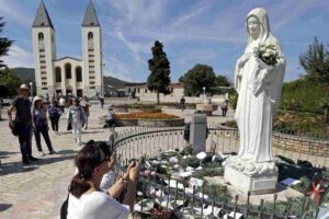 statua madonna di medjugorje con sfondo chiesa di medjugorje